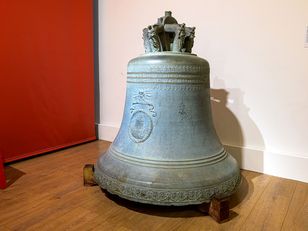 A large, antique bell with a green patina and a crown-like decoration