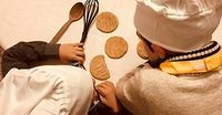 Deux enfants en toque de cuisinier face à des biscuits sur une table 
