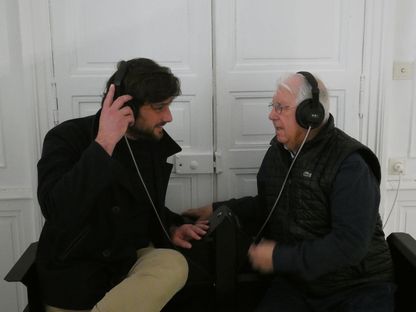 Deux hommes, un plus jeune et un plus âgé, partagent un moment d’écoute à une station sonore du Musée national de la Marine, illustrant la transmission intergénérationnelle.