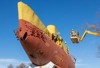 Vue du bathyscaphe FNRS III, engin sous-marin jaune et rouge de forme massive, installé en extérieur dans les jardins de la Tour Royale à Toulon, avec une nacelle élévatrice visible à l'arrière-plan.