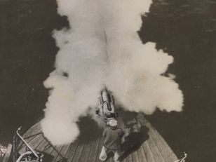 Photographie en plongée montrant un marin tirant au canon harponneur sur une baleine en mer, avec un panache de fumée blanche au moment du tir.