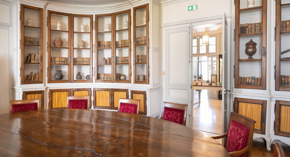 library room with a large wooden table in the center. The room has a curved wall with built-in bookshelves.