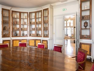 library room with a large wooden table in the center. The room has a curved wall with built-in bookshelves.
