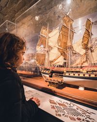 Visiteuse observant une maquette de navire ancien à voiles, exposée en vitrine dans une salle tamisée.