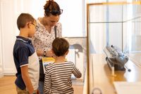 Une mère et ses deux enfants observent une maquette de sous-marin exposée dans une vitrine du musée national de la Marine à Rochefort, participant à une activité de médiation – photo Brumes Editions, 2024.