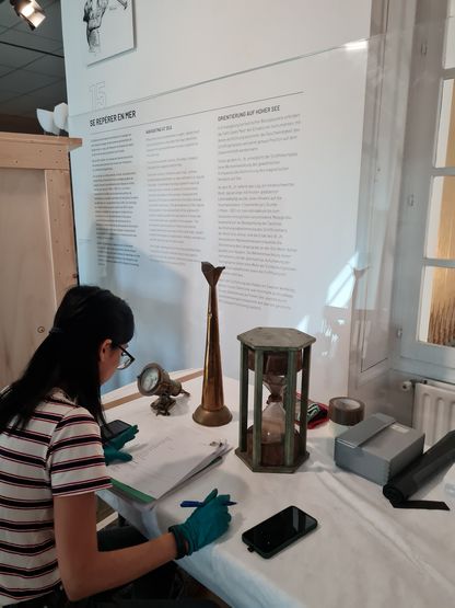 Agents du musée prenant des notes devant des instruments anciens : sablier, corne de brume, compas.