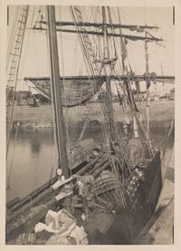 ue en plongée du pont d’un voilier amarré dans un port, chargé de barils et de filets, avec un enchevêtrement de mâts et de cordages – photographie en noir et blanc, début XXe siècle.