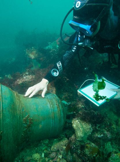 Archéologue plongeur étudiant une cloche de navire sur un site sous-marin, relevé d’observations lors d’une fouille archéologique subaquatique