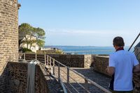 Visiteur observant la mer depuis les remparts d'un fort, bâtiments en pierre et vue dégagée sur l'horizon.