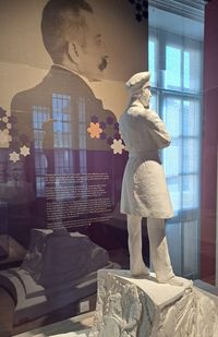 Maquette de monument représentant Julien Viaud, alias Pierre Loti, en uniforme de marin, de dos, sur un socle orné de bas-reliefs, exposée devant un portrait photographique de profil de l’écrivain au musée national de la Marine à Rochefort.
