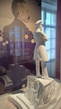 Maquette de monument représentant Julien Viaud, alias Pierre Loti, en uniforme de marin, de dos, sur un socle orné de bas-reliefs, exposée devant un portrait photographique de profil de l’écrivain au musée national de la Marine à Rochefort.