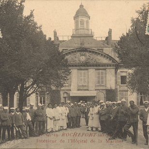 "Carte postale ancienne en noir et blanc montrant l’intérieur de l’Hôpital Maritime de Rochefort-sur-Mer : deux rangées de personnels (militaires en uniforme, infirmiers et aides-soignants en blouse et coiffe blanche) encadrent une allée centrale bordée d’arbres. En arrière-plan, la façade symétrique de l’hôpital, dotée d’un pavillon central à toit mansardé, de lucarnes et d’une horloge sculptée dans le fronton, ainsi qu’un auvent à l’entrée. Deux timbres-poste verts de 5 c. figurent dans les coins supérieurs, et en bas, en lettres rouges, la légende « V.G. 19. ROCHEFORT-sur-MER – Intérieur de l’Hôpital de la Marine »."