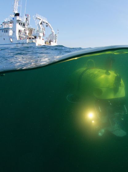 Photographie mi-air mi-eau montrant un navire en surface et un robot sous-marin HROV en mission de cartographie des fonds marins, campagne Ifremer 2018