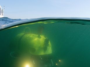 Photographie mi-air mi-eau montrant un navire en surface et un robot sous-marin HROV en mission de cartographie des fonds marins, campagne Ifremer 2018