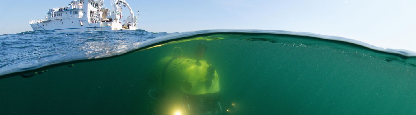 Photographie mi-air mi-eau montrant un navire en surface et un robot sous-marin HROV en mission de cartographie des fonds marins, campagne Ifremer 2018