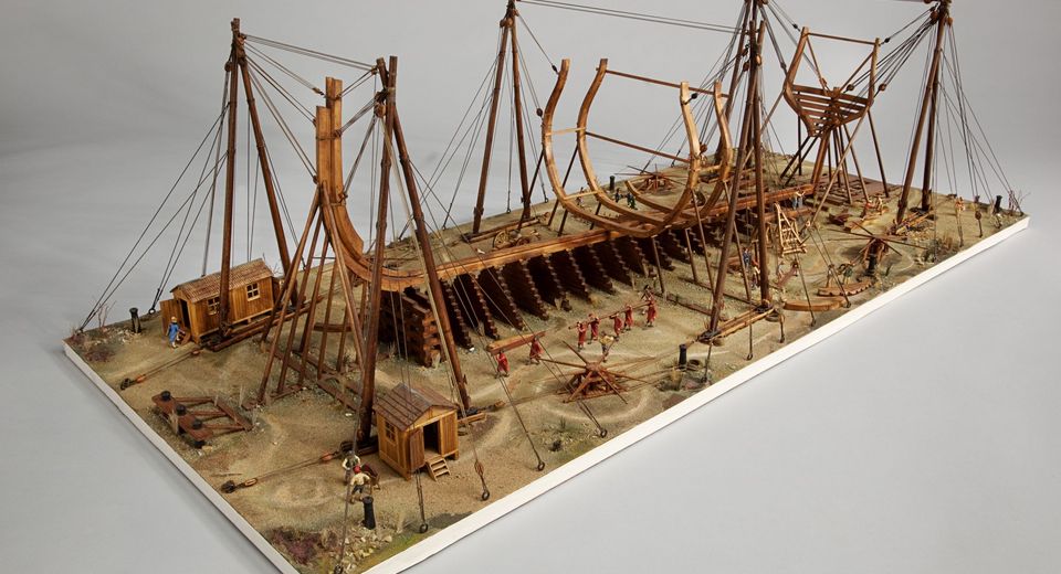 A miniature model of a shipyard with a wooden ship under construction, side view