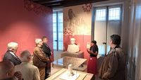 La commissaire de l'exposition présente les sculptures à un groupe de visiteurs dans une salle aux murs rouges ornée d’un décor évoquant l’île de Pâques.