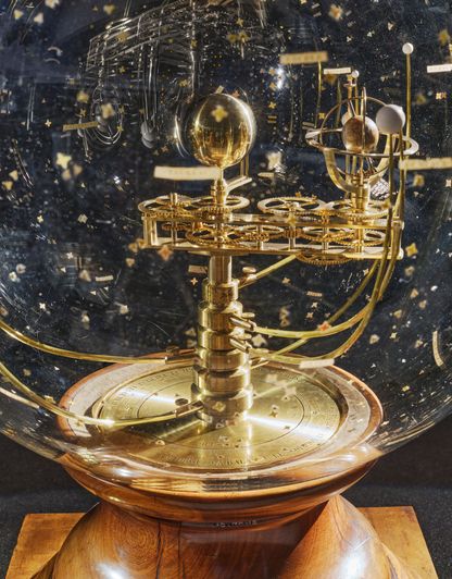 Détail du planétaire d’Émile Bertaux avec engrenages, globes et mécanisme en laiton illustrant les mouvements planétaires, constellations visibles en arrière-plan.
