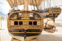 Vue de la poupe richement décorée d’un modèle d'instruction exposé au musée national de la Marine à Toulon, avec en arrière-plan d'autres navires miniatures et un câble enroulé.