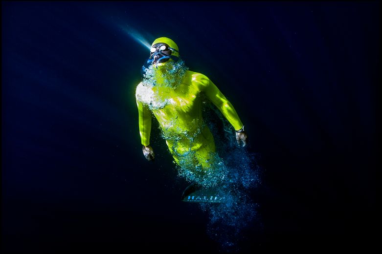Photographie sous-marine de Franck Seguin : un apnéiste en combinaison jaune fluo remonte vers la lumière, entouré de bulles, série « ABYSS ».
