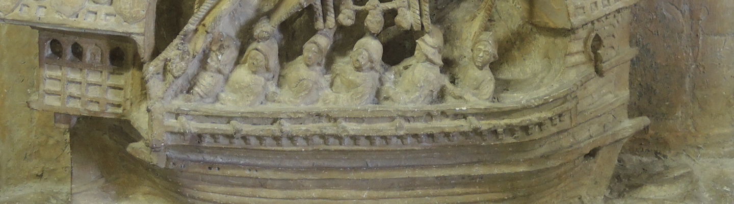 Détail d’une sculpture en pierre montrant la coque d’un bateau ancien, avec des rangées de rames, des personnages et des motifs décoratifs finement sculptés