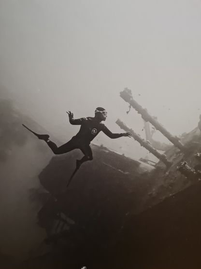 Détail de la photographie « ABYSS » de Franck Seguin : l'apnéiste en combinaison, palme tendue, évolue près des mâts brisés de l'épave.