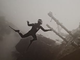 Détail de la photographie « ABYSS » de Franck Seguin : l'apnéiste en combinaison, palme tendue, évolue près des mâts brisés de l'épave.