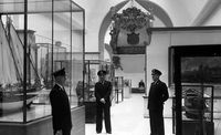 Photo en noir et blanc avec trois gardiens en tenu se tiennent devant les vitrines