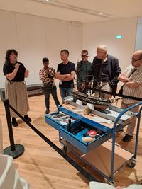 Présentation des métiers de la conservation au musée national de la Marine : un groupe de visiteurs échange avec une intervenante autour d’une maquette de navire et d’un chariot d’outils.