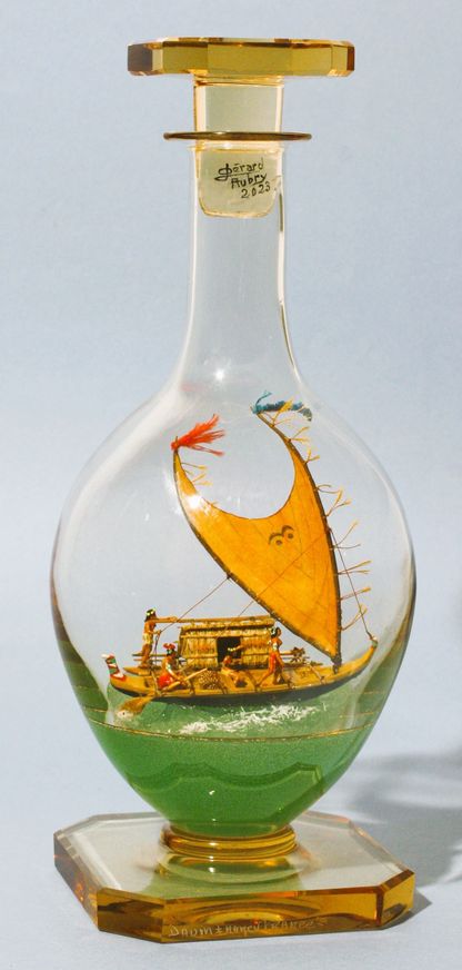 Modèle de pirogue traditionnelle mélanésienne dans une carafe en verre, avec voile triangulaire et équipage.