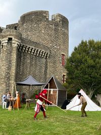 Deux personnages costumés simulent un combat avec des armes en bois, tandis que des artisans animent des stands historiques sous des tentes.