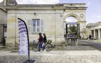 Une cycliste et un piéton devant l'entrée du musée