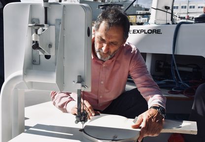 L'artiste Xavier Veilhan découpe une pièce de bois à l’aide d’une scie à ruban installée sur le catamaran We Explore.