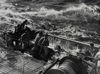 Marins en ciré manœuvrant sur le pont d’un bateau de pêche en pleine mer agitée, sous les assauts des vagues – photographie en noir et blanc, milieu du XXe siècle.