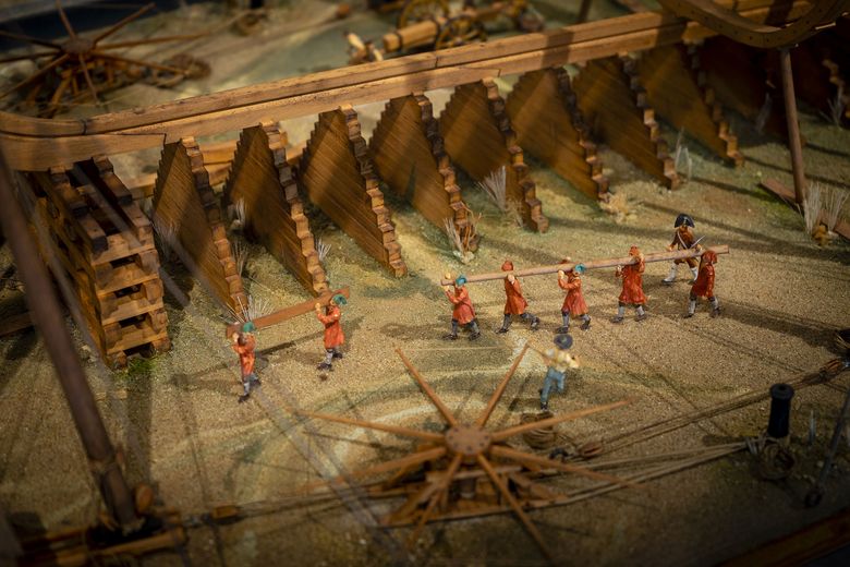 A miniature model of a wooden structure with a thatched roof and workers in orange and blue overalls