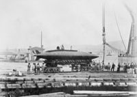 Essais du sous-marin Gymnote en 1888, prototype posé sur un quai avec équipage et grue en arrière-plan, photographie en noir et blanc.