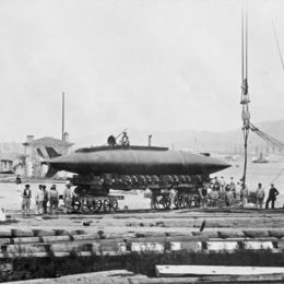 Essais du sous-marin Gymnote en 1888, prototype posé sur un quai avec équipage et grue en arrière-plan, photographie en noir et blanc.