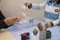 Atelier créatif pour enfants au musée national de la Marine, où un enfant construit un bateau en papier accompagné d’un adulte, entourés de crayons et matériel de dessin.