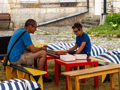 Un adulte et un enfant jouent ensemble à un jeu éducatif en plein air dans la cour du musée national de la Marine, assis sur des bancs colorés.