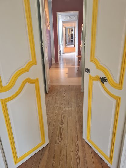 Vue en perspective d’une enfilade de salles réaménagées avec portes blanches et moulures dorées au musée national de la Marine à Rochefort.