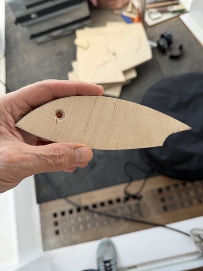 Main tenant une petite sculpture en bois clair en forme de poisson, réalisée à bord du voilier We Explore.