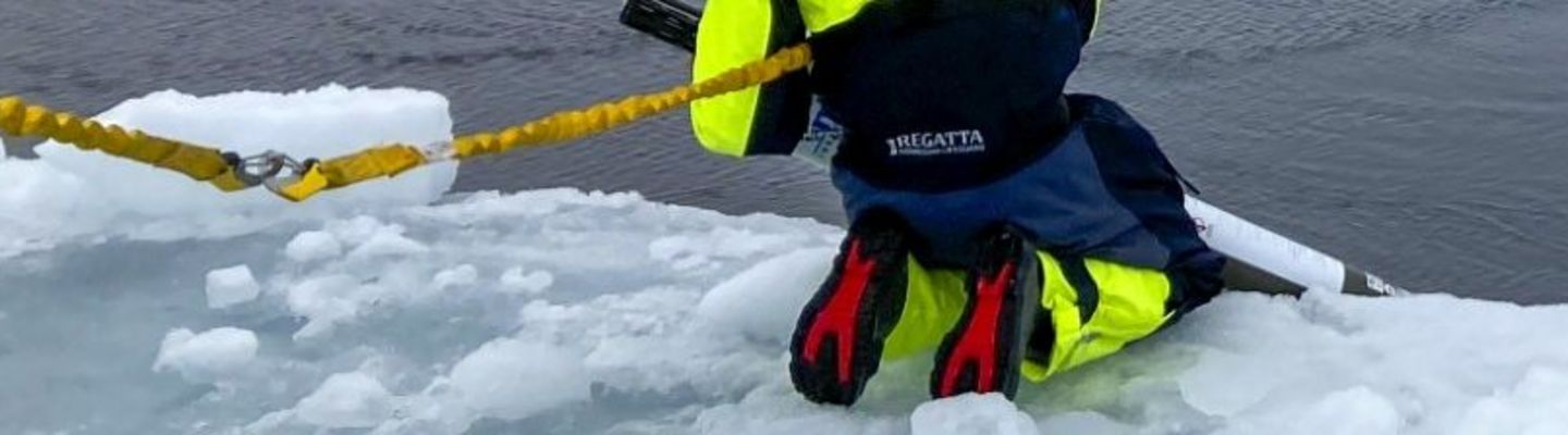 Océanographe en combinaison de sécurité effectuant des relevés sur la banquise arctique, face à un navire dans le brouillard, en mer de Kara.