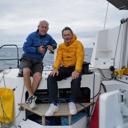 Xavier Veilhan et Roland Jourdain à l’arrière du catamaran We Explore, en mer, vêtus de tenues techniques, regardant l’objectif.