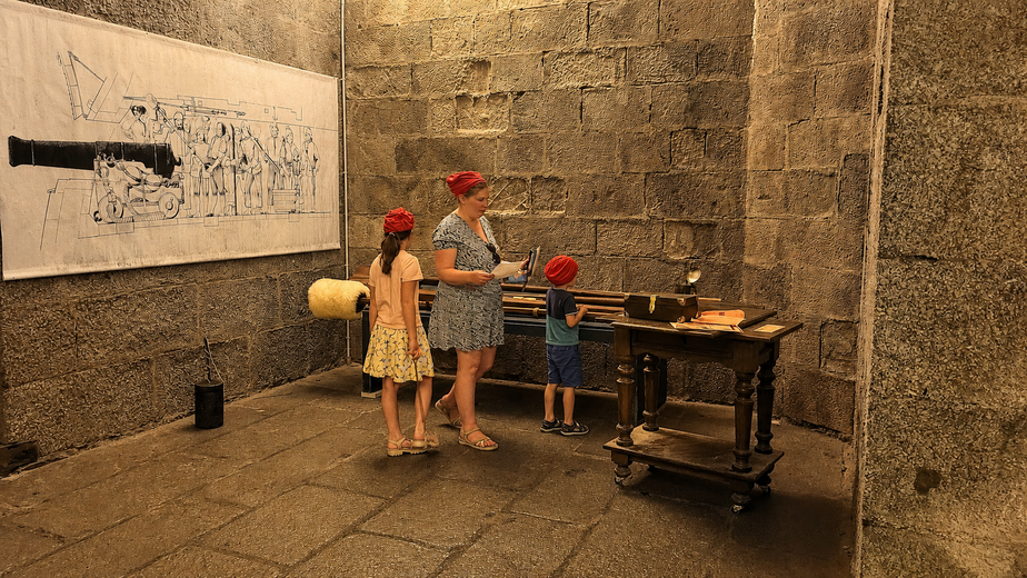 Une famille résout des énigmes autour d'une table en bois chargée d'accessoires d'époque, dans une salle voûtée en pierre du château de Brest lors de l'escape game Les évadés du château