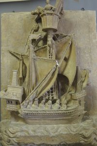 Sculpture en relief montrant un grand bateau ancien avec un mât, des voiles et des décorations, entouré de motifs sculptés dans la pierre