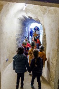 Groupe de visiteurs dans un couloir voûté en pierre, avançant vers une salle d'exposition éclairée.