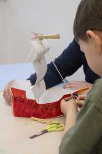Enfant et adulte assemblant un navire en papier lors de l’atelier « Toutes voiles dehors ! » au musée national de la Marine à Toulon.