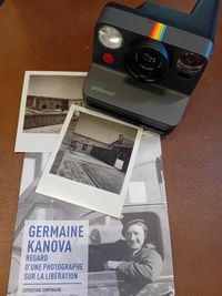 Appareil photo Polaroid posé sur une table avec deux clichés en noir et blanc et une brochure de l’exposition Germaine Kanova.