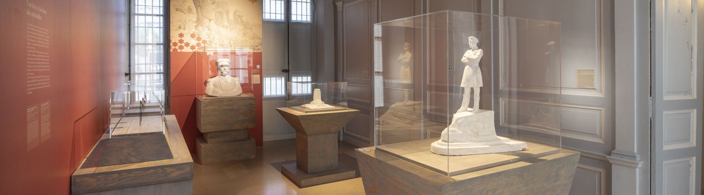 Salle d’exposition consacrée à Pierre Loti au musée national de la Marine de Rochefort, présentant des sculptures et objets dans une scénographie aux tons sobres et éclairages ciblés.