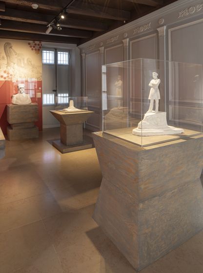 Salle d’exposition consacrée à Pierre Loti au musée national de la Marine de Rochefort, présentant des sculptures et objets dans une scénographie aux tons sobres et éclairages ciblés.